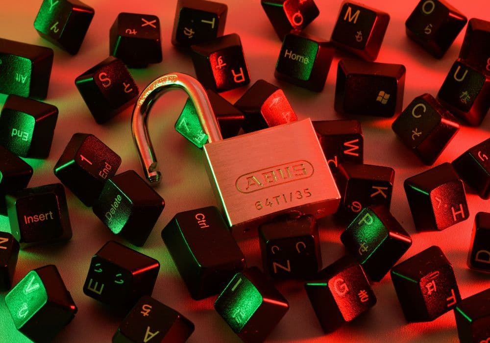 An open padlock lying on a keyboard with keys scattered about