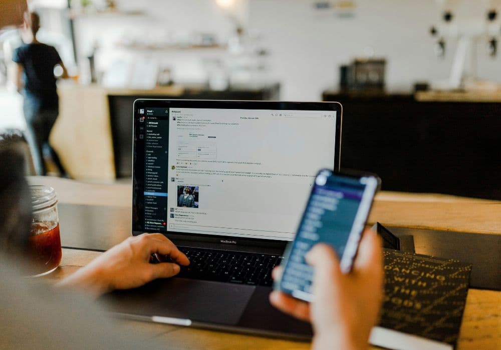 Person working on laptop and using smartphone in a café workspace